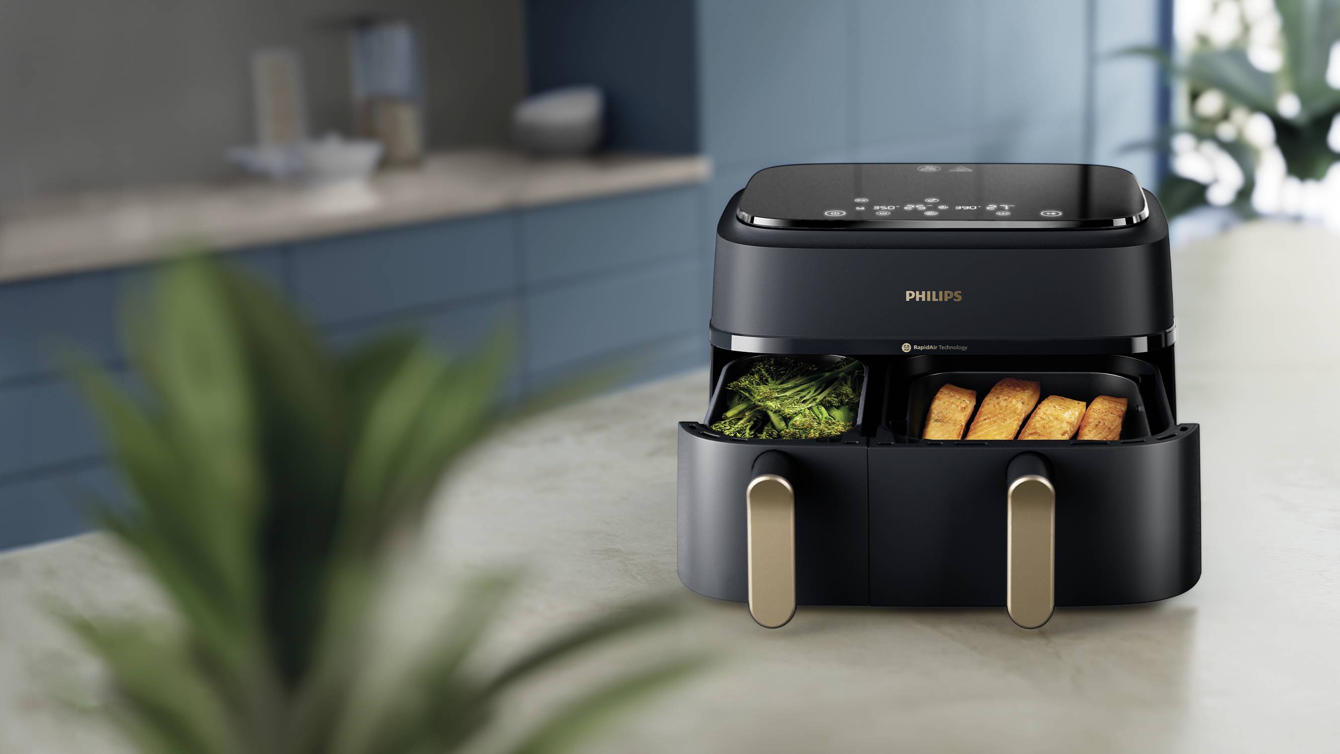 Een zwarte airfryer met twee compartimenten staat op een aanrecht. In de compartimenten zijn groenten en friet te zien.