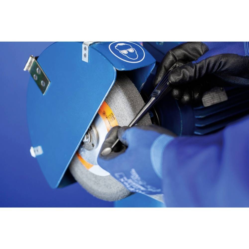 Een persoon in blauwe beschermende kleding bedient een slijpmachine, waarbij een gereedschap wordt bewerkt. De focus ligt op arbeidsveiligheid en precisie.