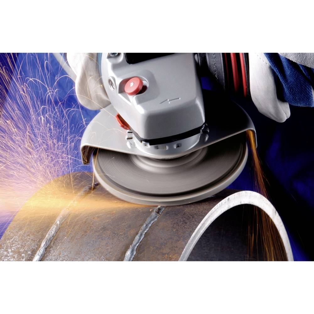 Een arbeider gebruikt een haakse slijper om metaal te bewerken. Vonken vliegen door de lucht terwijl het gereedschap over de buis glijdt.