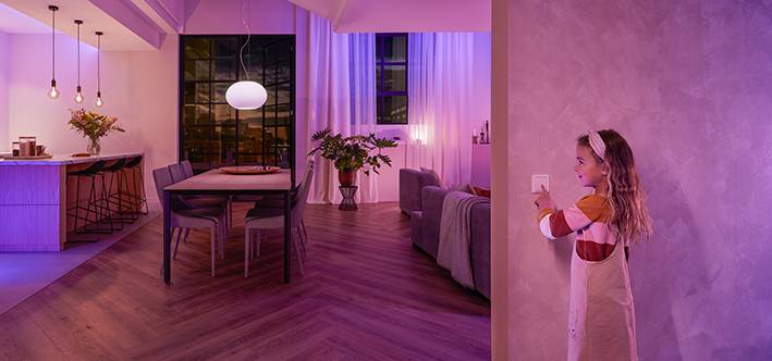 Een kind schakelt het licht aan in een modern ingericht woonkamer. De ruimte is uitgerust met een eettafel, stoelen en planten.