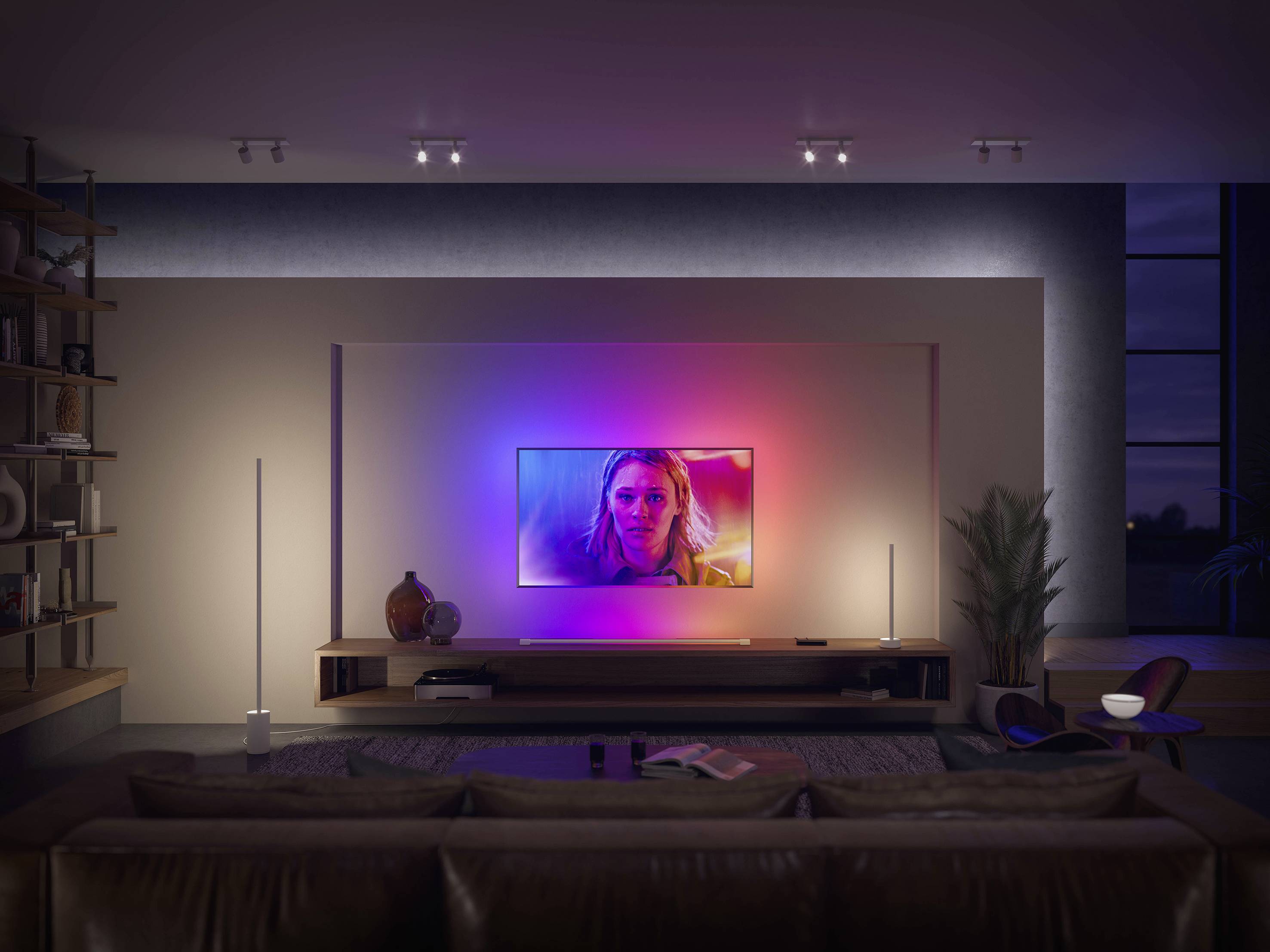 Een woonkamer met een grote televisie aan de muur die aanstaat. De ruimte is modern ingericht en zacht verlicht.