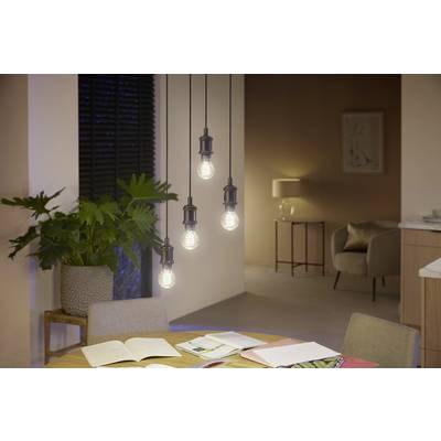 Eetkamer met een ronde tafel en vier hangende lampen boven boeken, op de achtergrond zijn een fauteuil, een staande lamp en een plant te zien.