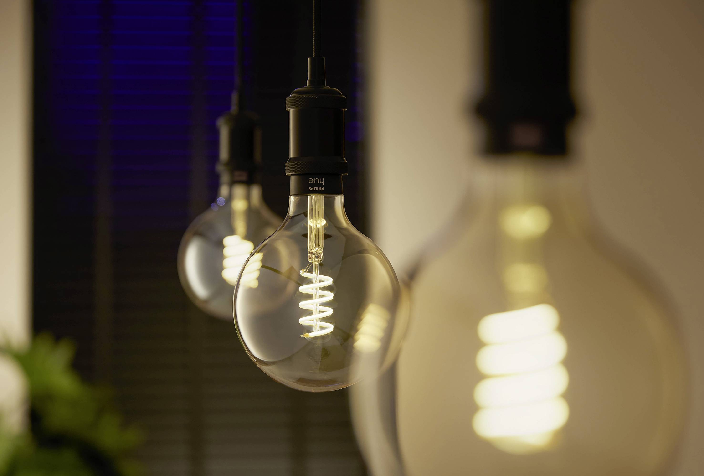 Drie brandende gloeilampen hangen van het plafond, waarbij de structuren van de gloeidraad zichtbaar zijn. Op de achtergrond zijn jaloezieën.