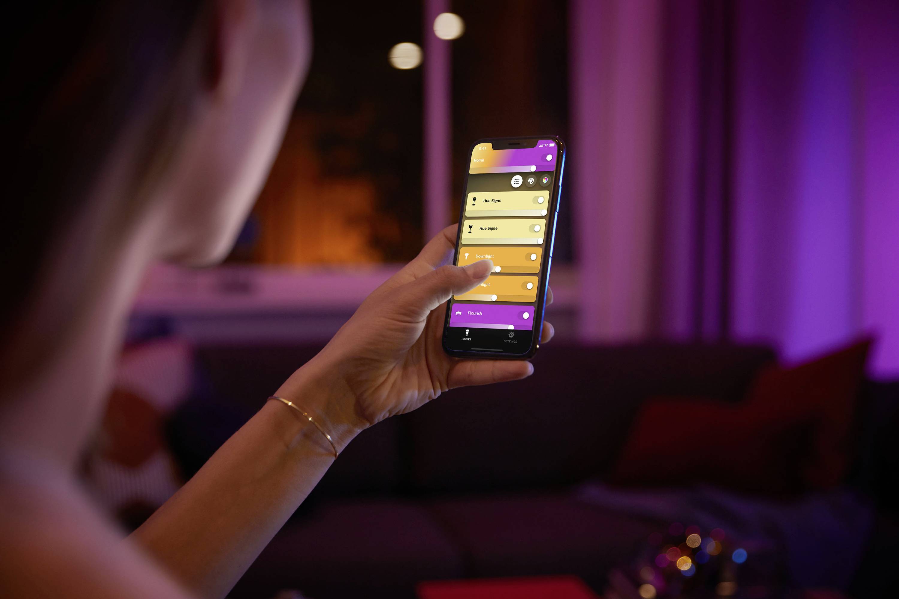 Een persoon bedient via een smartphone-app de verlichting in een gezellig verlicht woonvertrek.