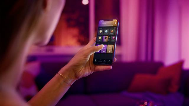 Een persoon bedient een smartphone in een sfeervol verlichte ruimte. Op het scherm zijn meerdere apps zichtbaar.