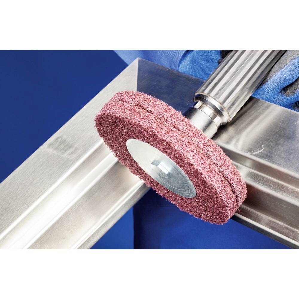 Een roterende slijpschijf polijst het oppervlak van een roestvrij stalen onderdeel. Handschoenen beschermen de handen van de operator.