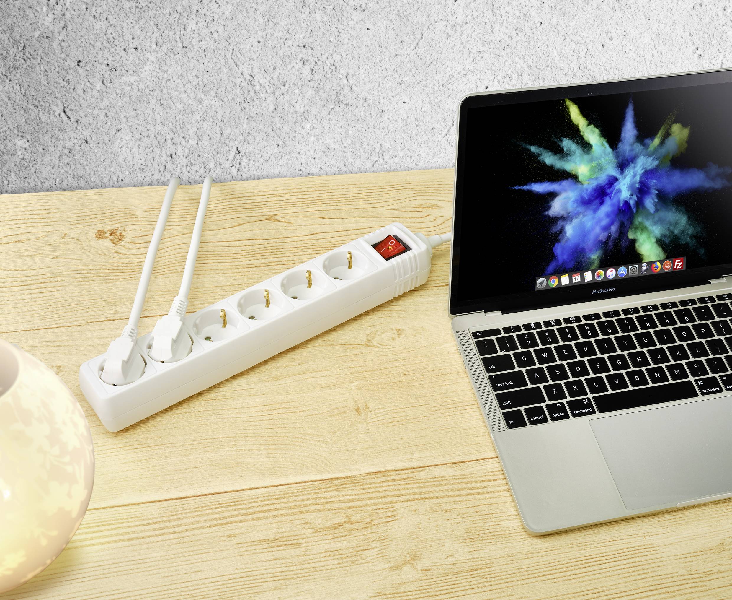 Laptop naast een stekkerdoos met twee aangesloten kabels op een houten tafel. Het scherm toont een kleurrijke grafiek.