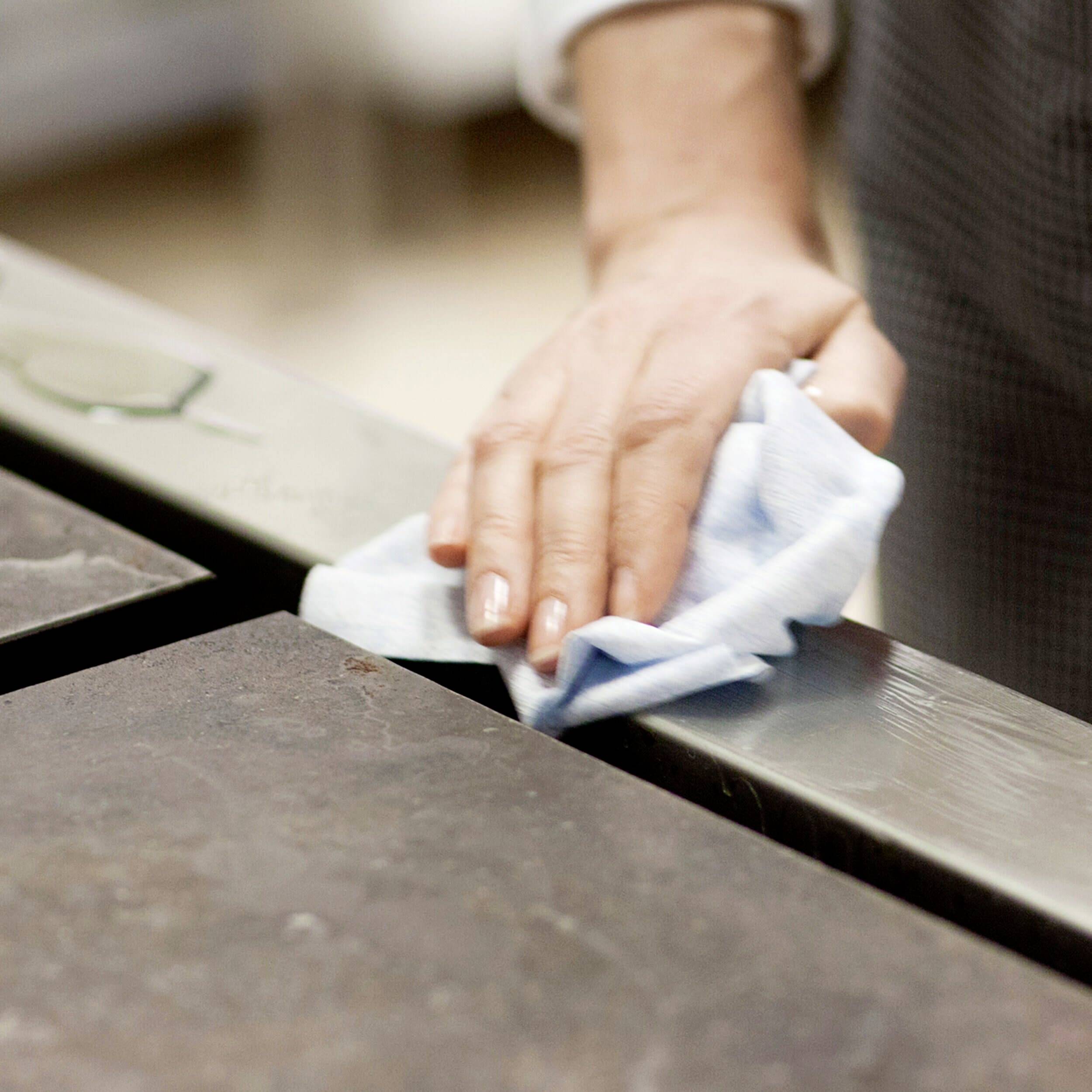 Een hand veegt met een blauwe doek over een donker tafeloppervlak.