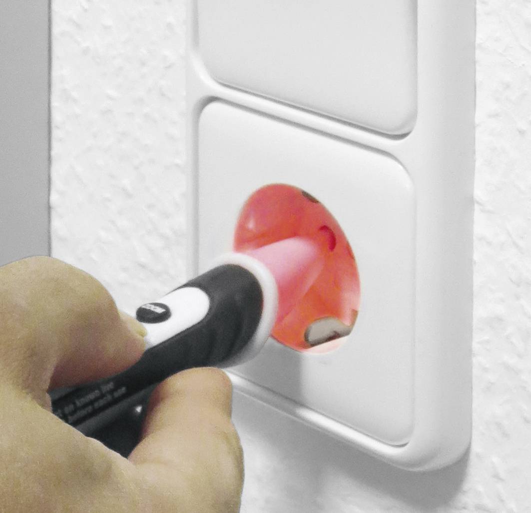 Een hand test een stekkerdoos met een spanningzoeker. De tester licht rood op, wat wijst op elektrische spanning.