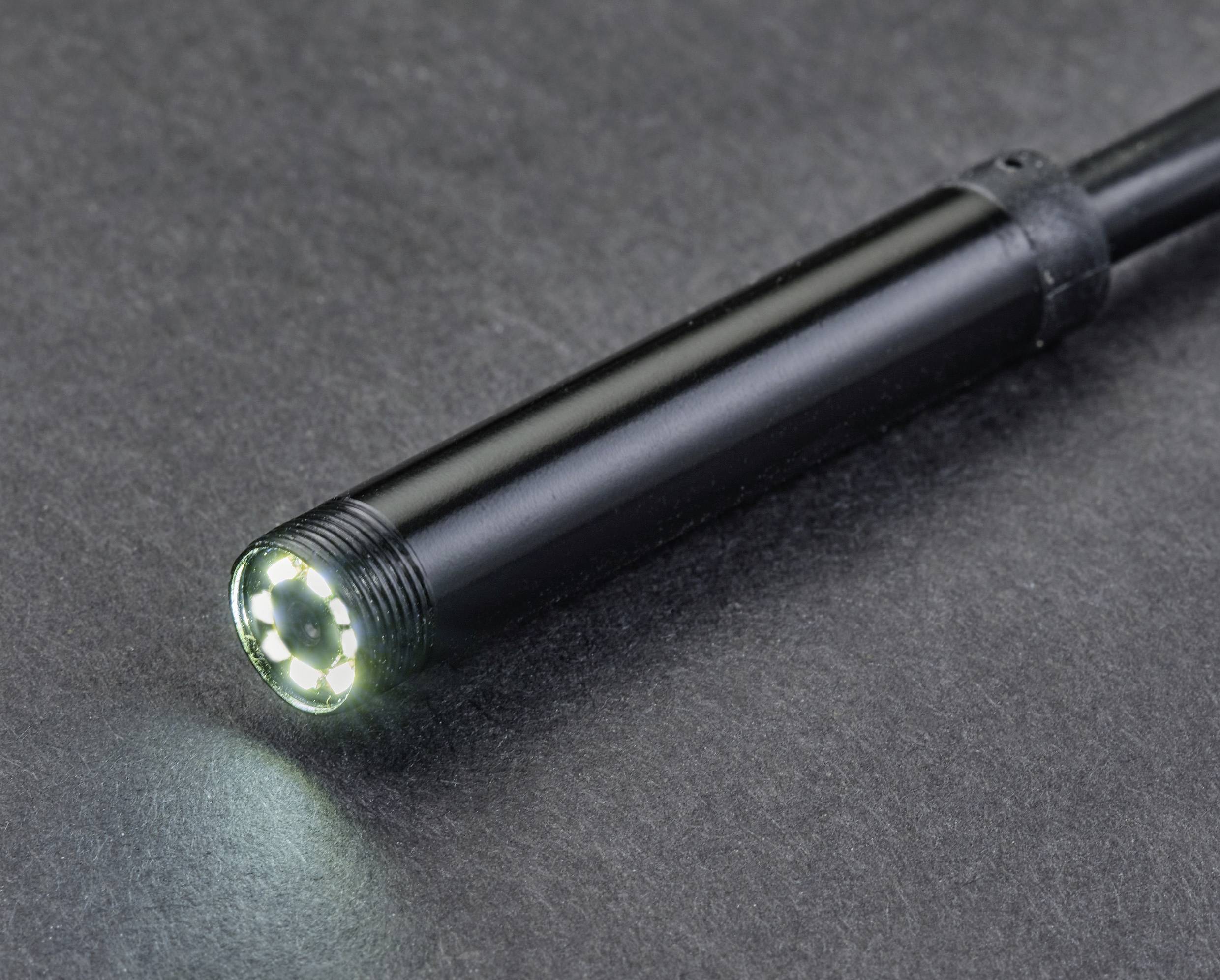 Close-up van een zwart endoscoop met oplichtende LED-lampjes aan de punt, liggend op een grijze achtergrond.