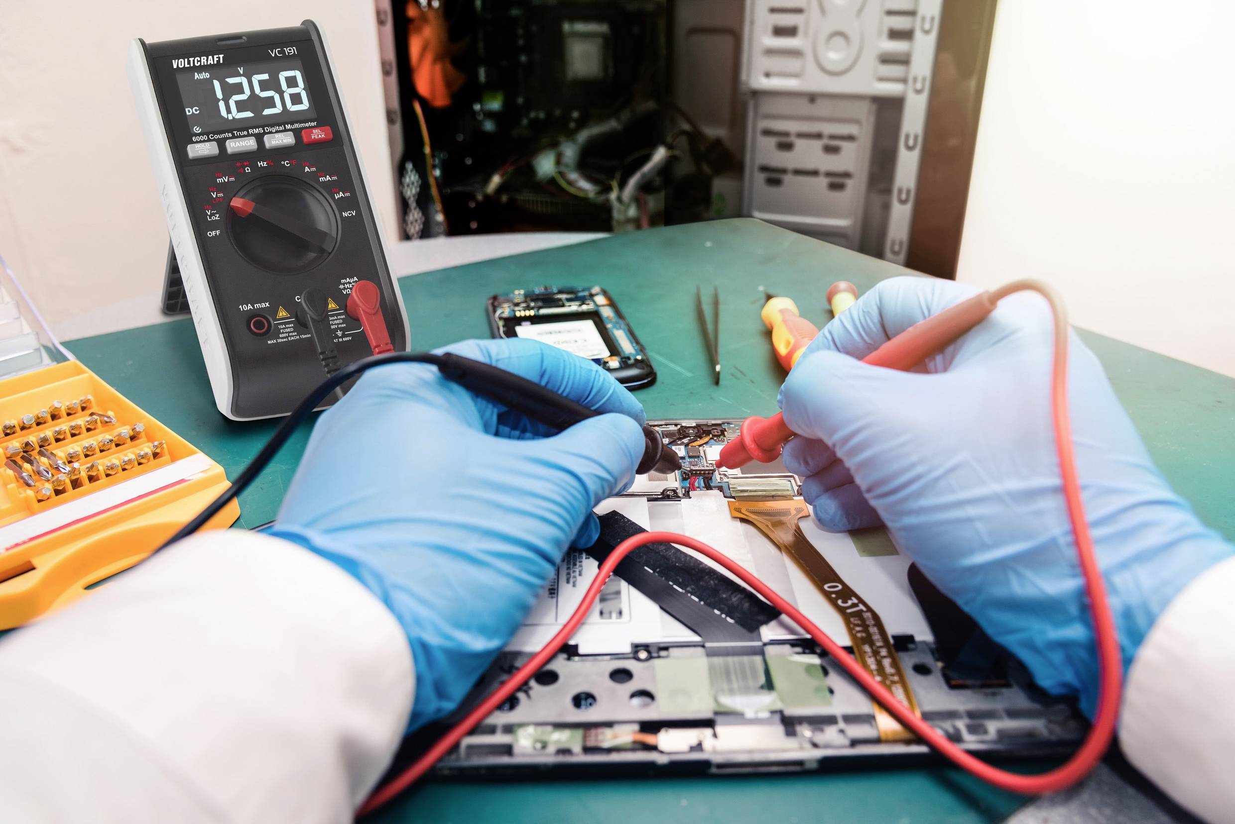 Een persoon met blauwe handschoenen repareert een elektronisch apparaat met een multimeter. Op de achtergrond zijn gereedschappen zichtbaar.