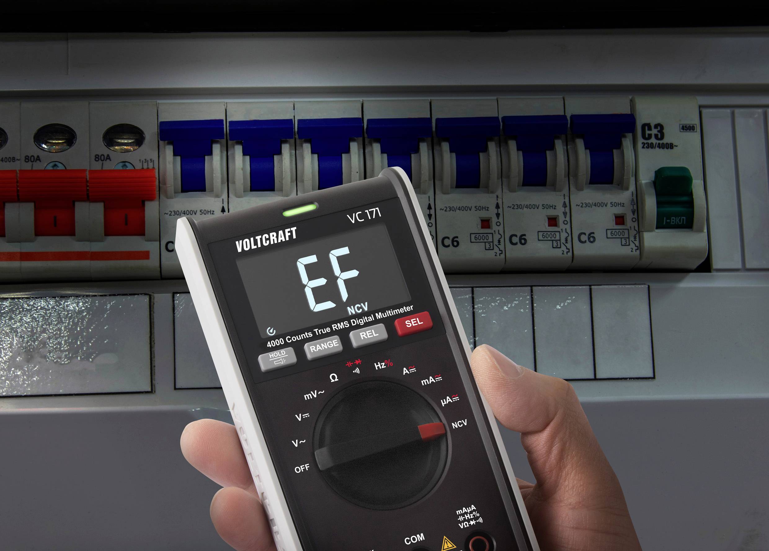 Een persoon houdt een multimeter vast die de foutcode EF weergeeft. Op de achtergrond is een elektriciteitskast zichtbaar.