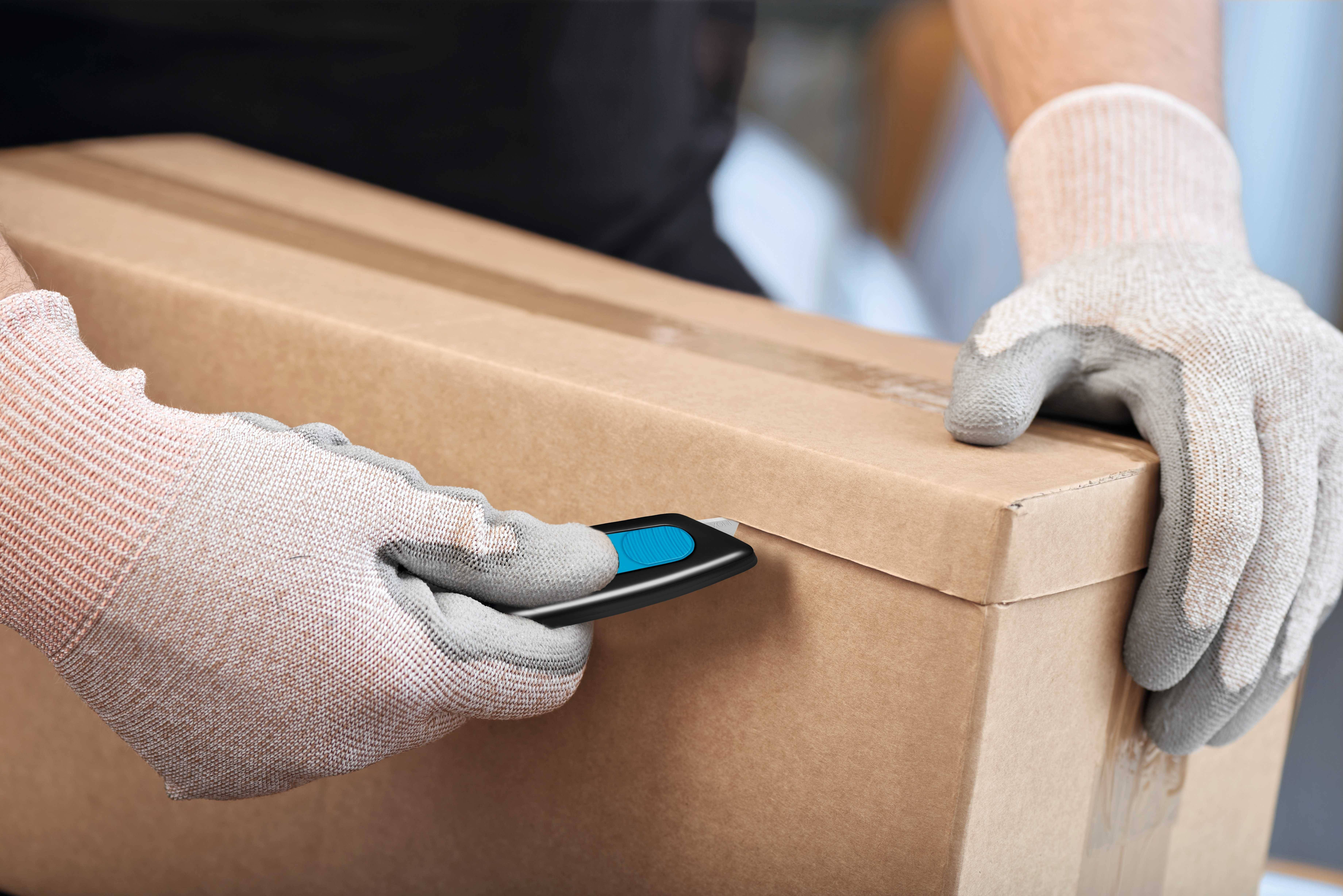 Een persoon draagt handschoenen en opent een kartonnen doos met een stanleymes.