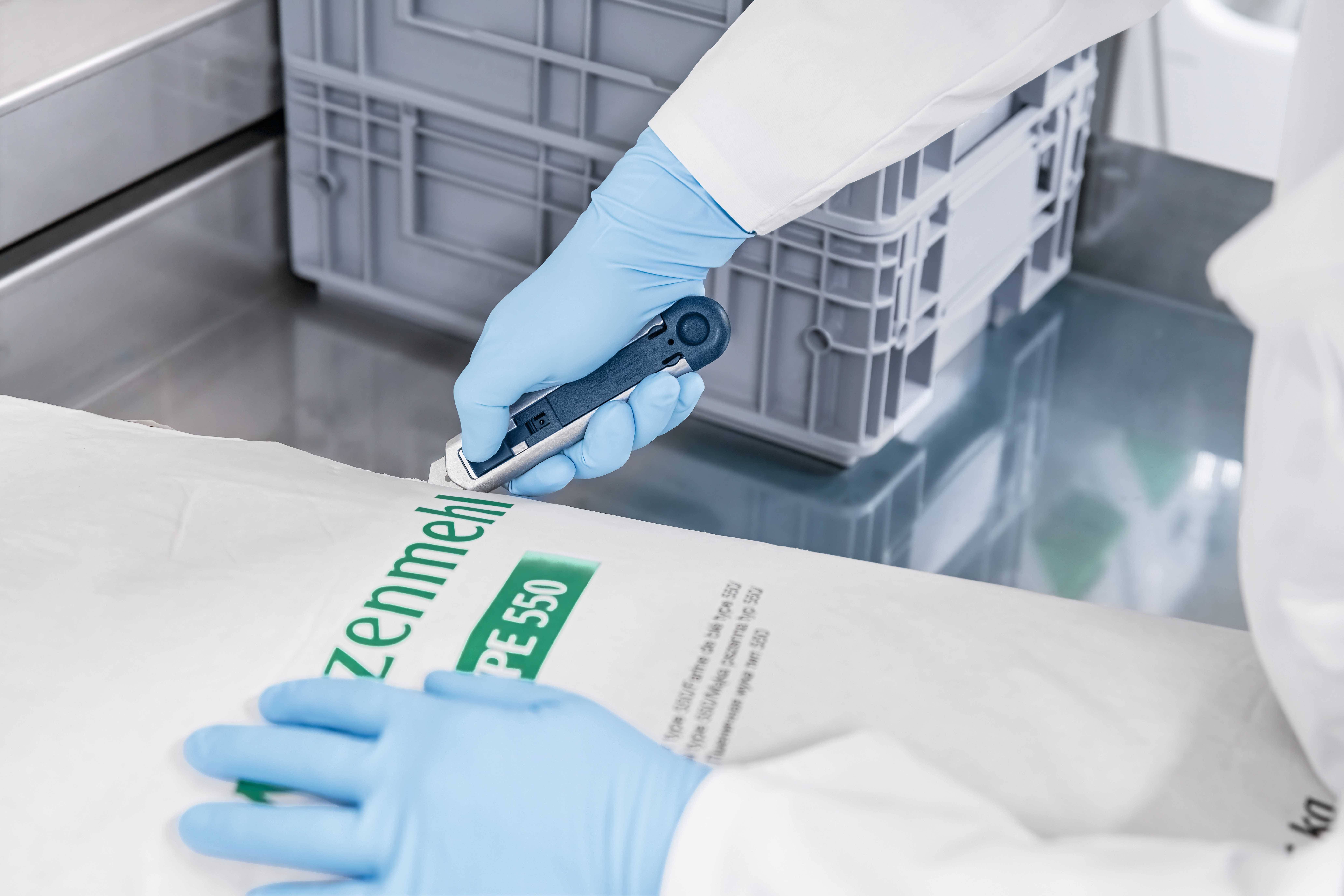 Een persoon in laboratoriumkleding inspecteert een verpakking met het opschrift 'Tarwemeel Type 550' in een laboratoriumomgeving.