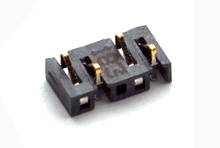 Kleine zwarte kunststof stekker met drie gouden contactpunten, liggend op een wit oppervlak. Elektronisch onderdeel.
