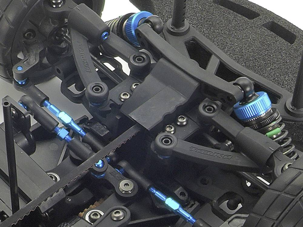 Een close-up van een RC-auto toont een gedetailleerd onderstel met schokdempers, blauwe schroeven en een riemensysteem.