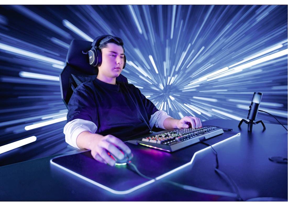 Een persoon zit met koptelefoons bij een computer met een futuristische achtergrondverlichting die beweging en snelheid suggereert.