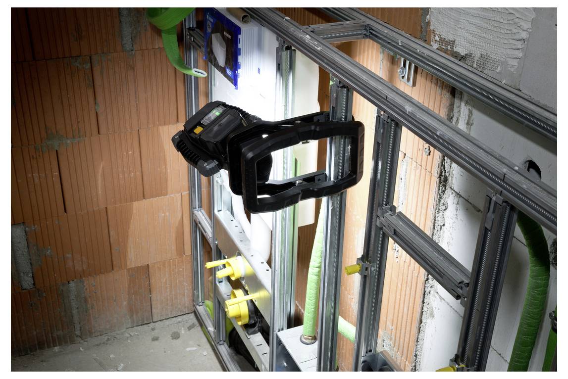 Bouwplaats interieur met metalen frames en wandpanelen, met een gemonteerd zwart apparaat en groene buizen in een onafgewerkt vertrek.