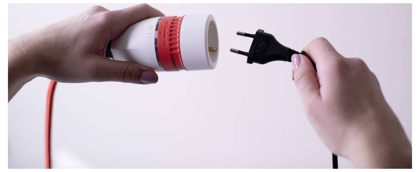 Handen die een stroomkabel met stekker op het stopcontact van een elektrisch apparaat aansluiten, wat aangeeft dat het apparaat wordt ingestopt of ingeschakeld.