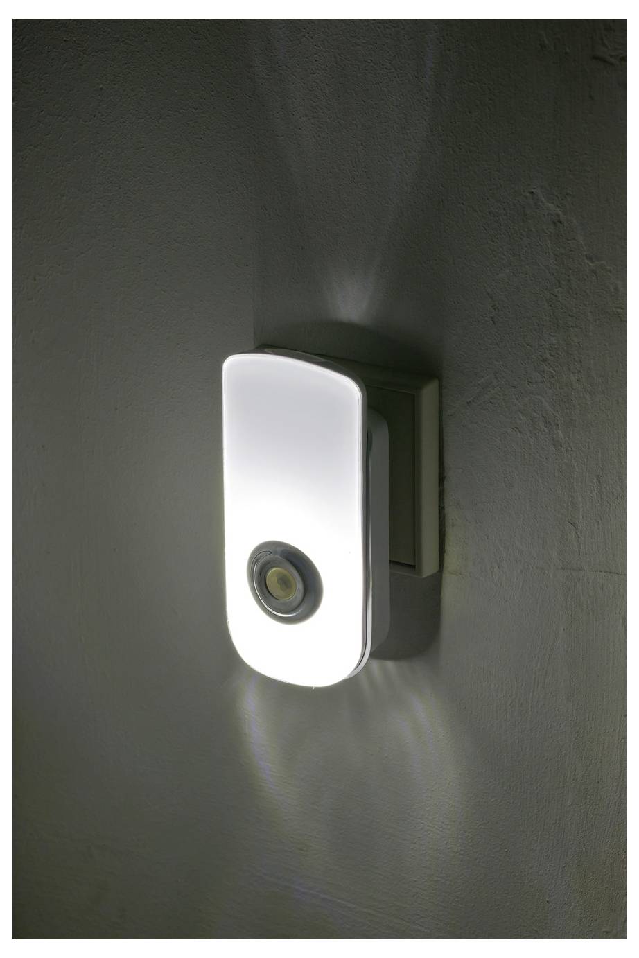Aan de muur gemonteerd nachtlampje met een gloeiend wit frontpaneel en circulaire sensor, die zacht licht op een donkere muur uitstraalt.