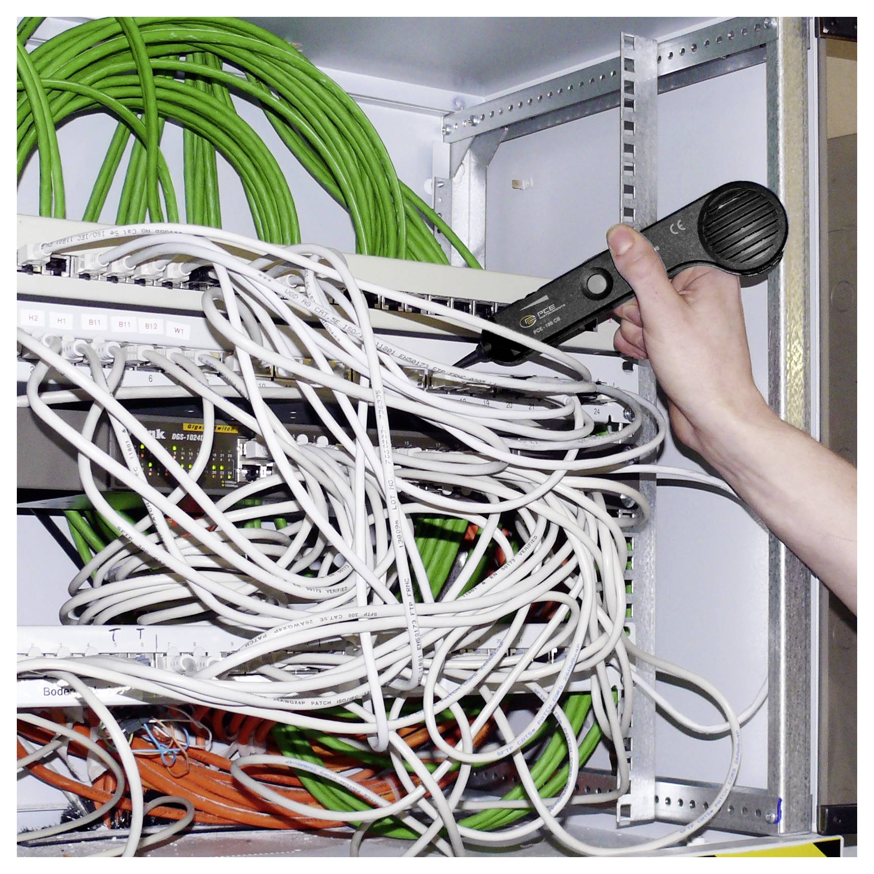 Hand die een kabeltoetser vasthoudt, controleert een warrige netwerk van draden in een serverrakaast.