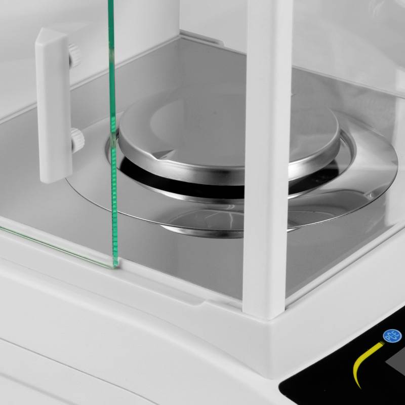 Een precisieweegschaal met een rond metalen plateau in een doorzichtige behuizing, geschikt voor nauwkeurige metingen in laboratoria.
