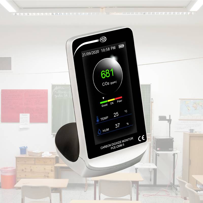 Een CO2-meter op een tafel in een klaslokaal. Het scherm toont de CO2-concentratie in ppm, evenals temperatuur en luchtvochtigheid.