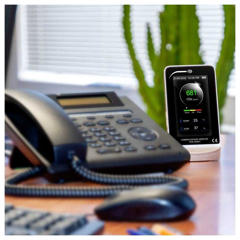 Kantoorafel met een telefoon en een kooldioxide-monitor die 681 ppm aangeeft, plus temperatuur- en vochtigheidsmeting.