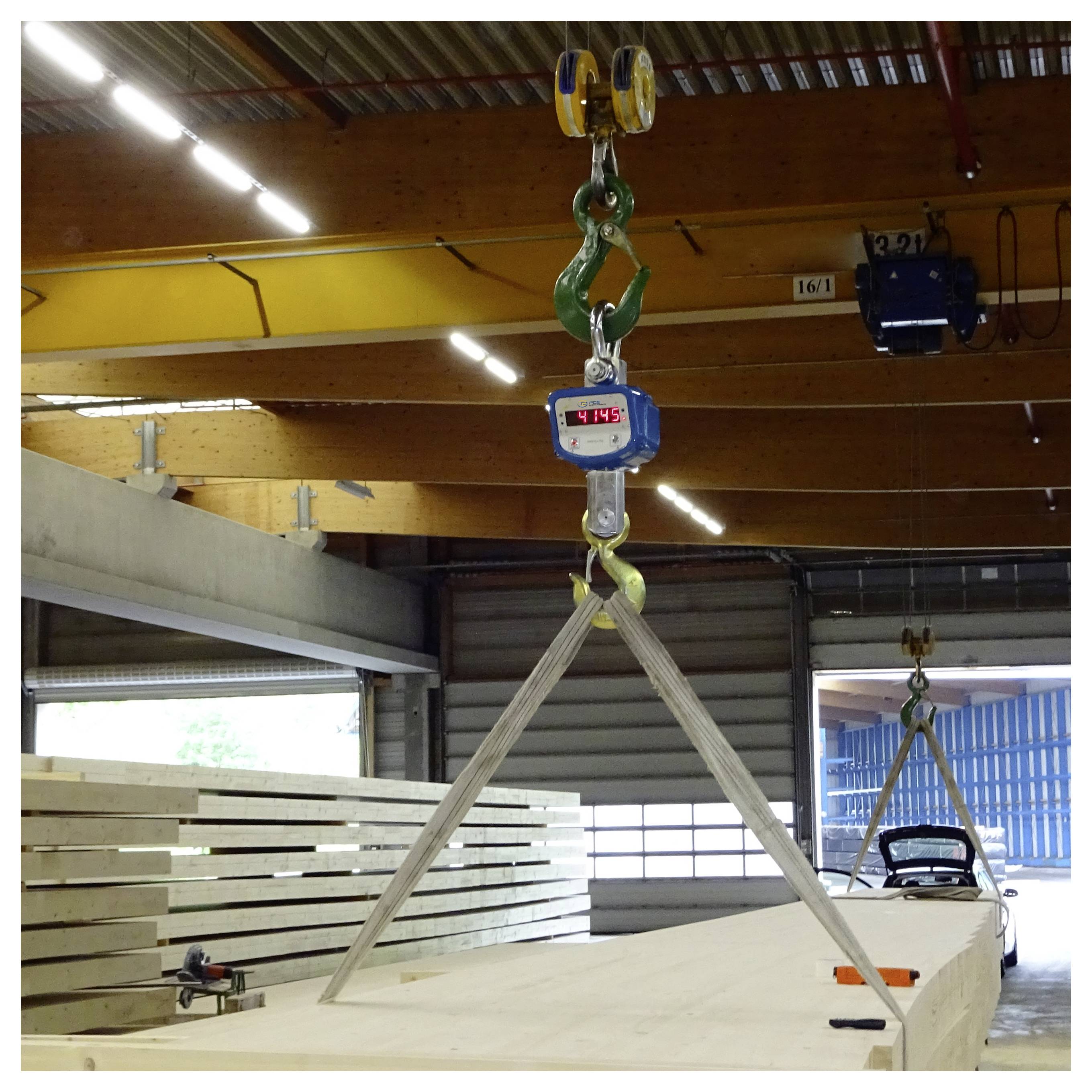 Overheadkraan tilt een grote houten balk met slingers in een werkplaats op, gewicht weergegeven op de hijskraan.