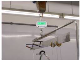 Hangend digitaal kraanweegschaal met een groen verlicht display opgehangen aan een bovenbalk in een industriële omgeving.
