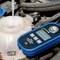 Een digitale refractometer meet de concentratie van een vloeistof in een container in de motorruimte van een auto.