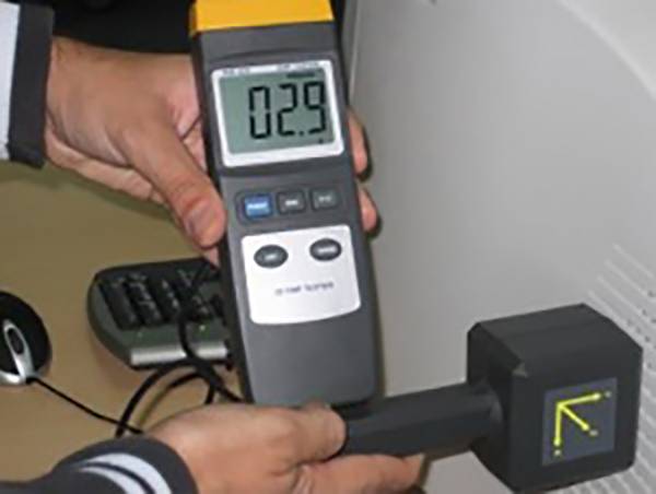 'Een persoon houdt een elektronisch meetapparaat met een display dat 0,29 aangeeft, dicht bij een computerscherm om straling te meten.'