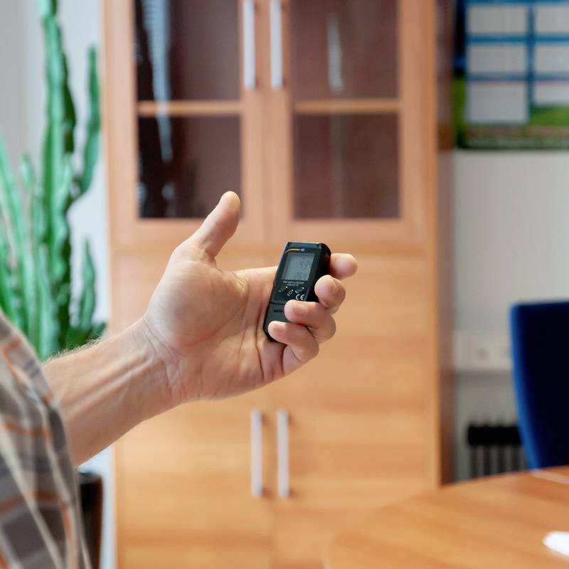 Een hand houdt een mobiele telefoon vast in een kantoor met houten meubels en planten op de achtergrond.