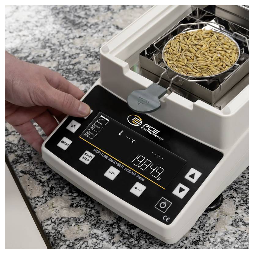 Hand die een graanvochtanalysator bedient met een voorbeadbakje met tarwe erop, waarop een digitaal percentageweergave op het display wordt getoond.