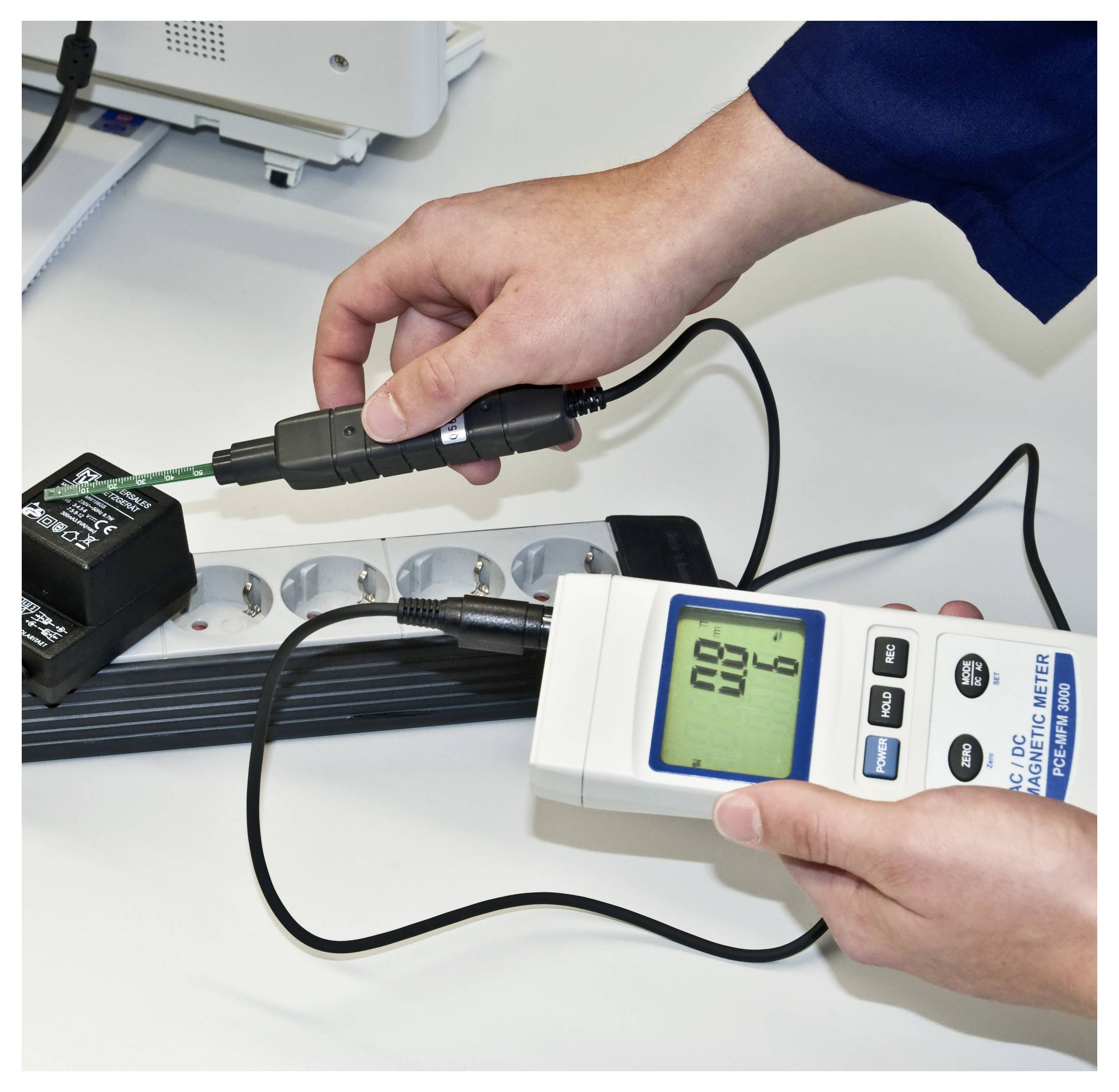 Een persoon die elektrische output meet met een handheld meter die is verbonden met een apparaat op een werkbank.