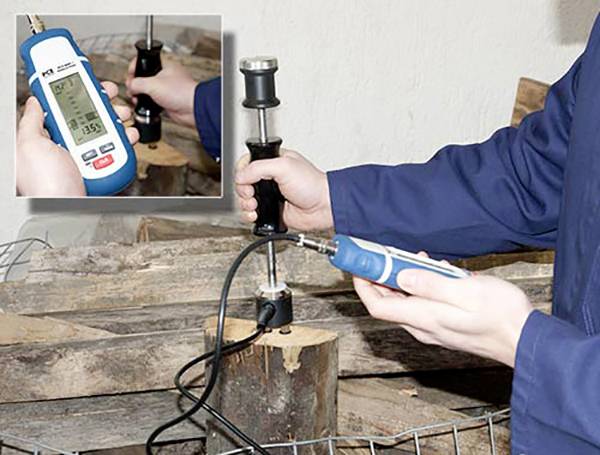 Een persoon meet het vochtgehalte van brandhout met een digitale vochtmeter die op een stuk hout is geplaatst.