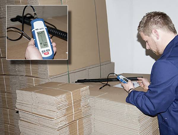 Een man controleert de luchtvochtigheid in een stapel golfkarton met een digitale hygrometer.
