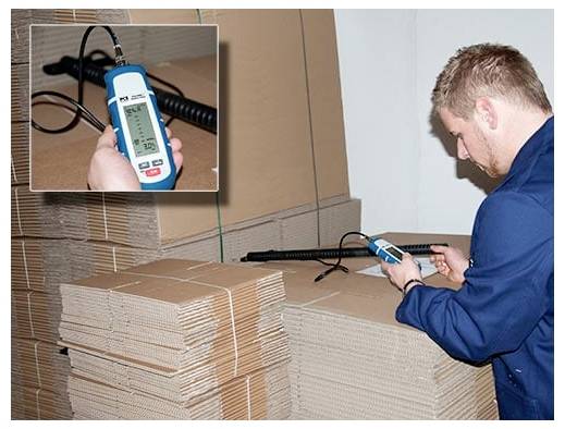 Een werker meet gestapelde kartonnen vellen met een draagbaar digitaal apparaat, met een close-up inzet van het meterweergave.