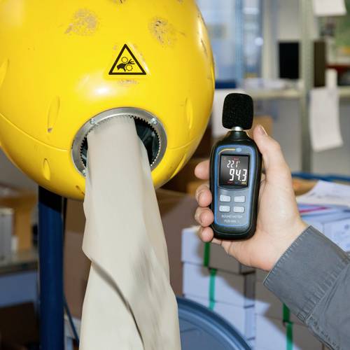 Een persoon houdt een thermometer vast die 22,7°C aangeeft, naast een machine die meel produceert. Een waarschuwingssymbool is op de machine aangebracht.