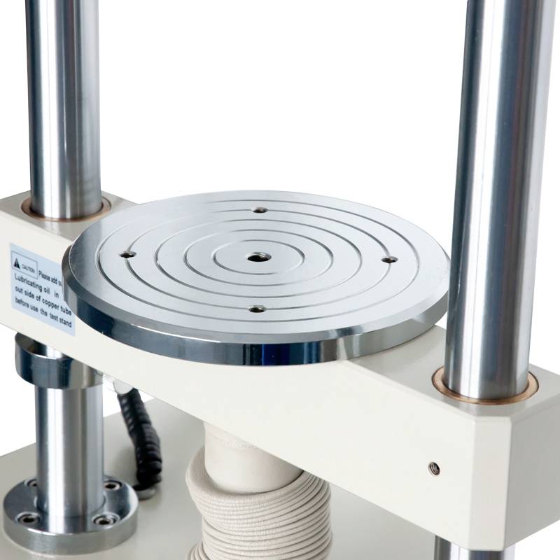 Een platenspeler met een ronde metalen schijf en zilveren steunpilaren op een witte voet.