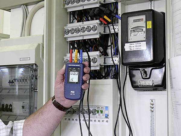 Een persoon meet het stroomverbruik van een elektrische schakelkast met een draagbaar meetapparaat.