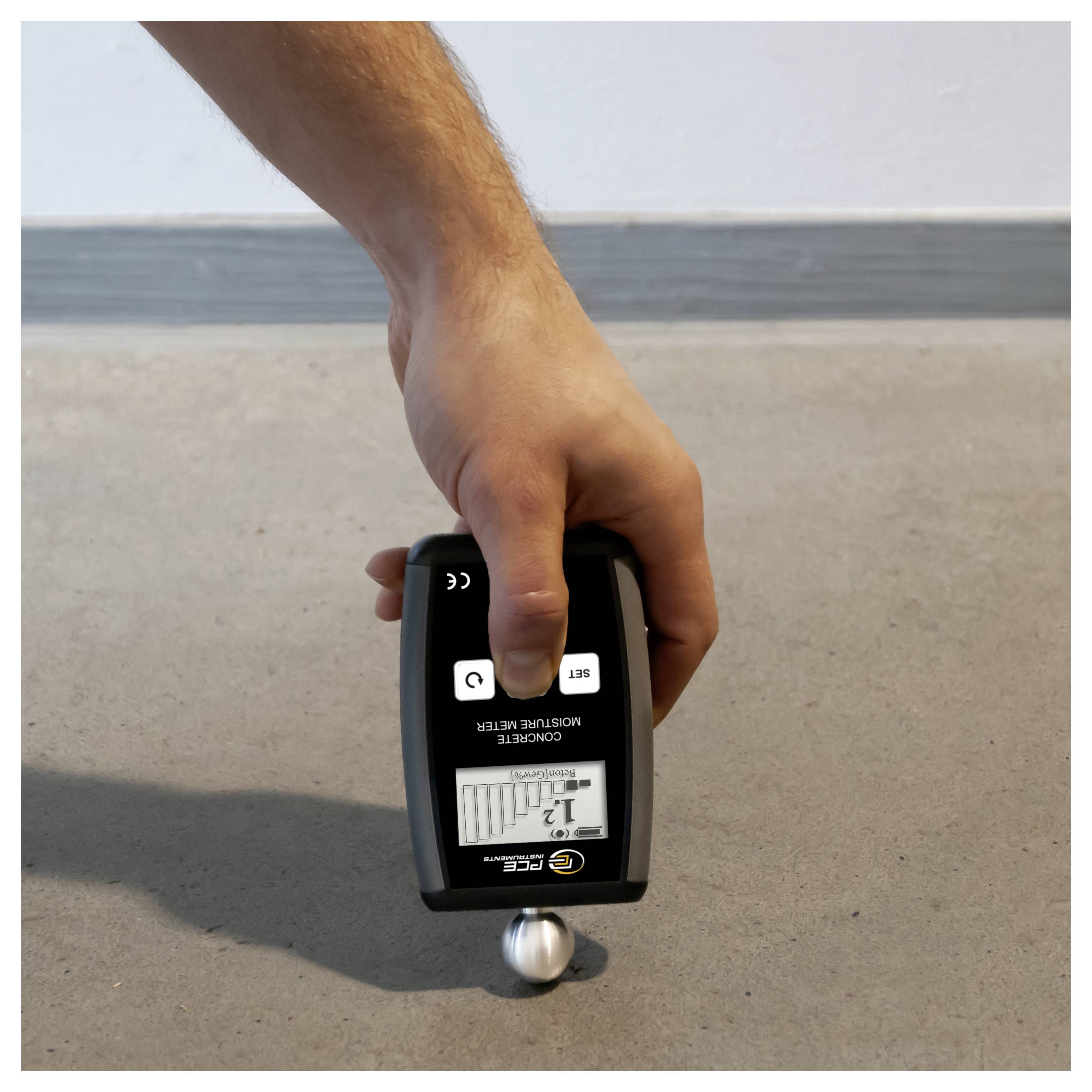 Hand die een digitale coating dikte meter tegen een metalen bal op de vloer houdt, om oppervlaktedikte of materiaaldiepte te controleren.