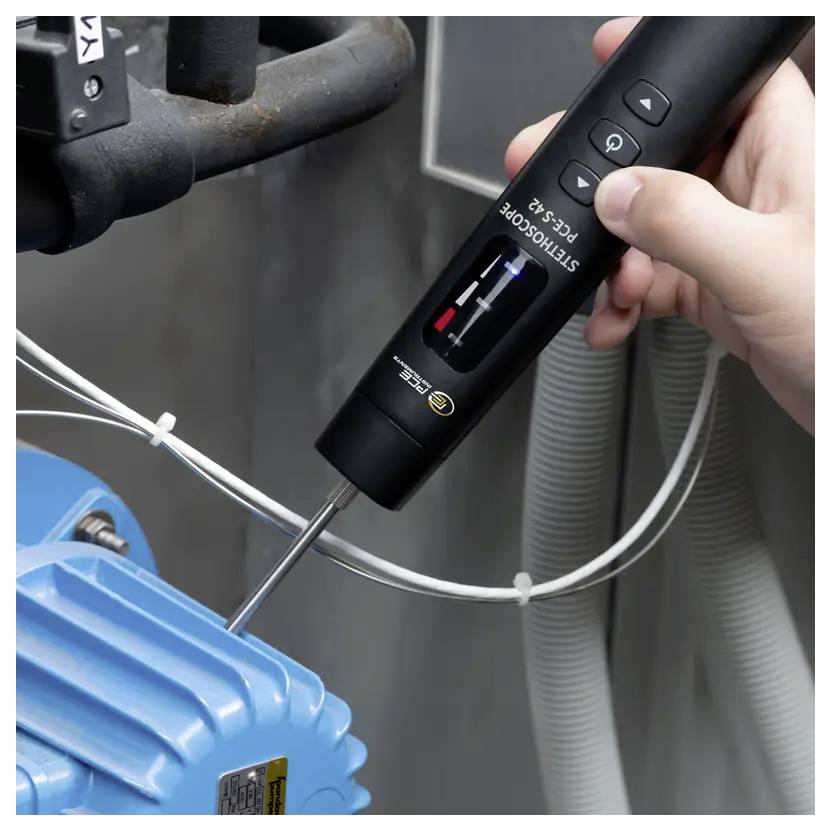 Een persoon gebruikt een handheld oscilloscoopprobe op een blauwe industriële machine om trillingen te meten, met een display en bedieningsknoppen.