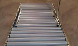 Transportband met metalen rollen in een magazijn. Het lijkt ongebruikt en klaar voor goederen- of materiaalvervoer.