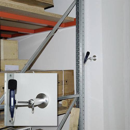 Een geluidsniveaumeter is bevestigd aan een metalen frame en meet het geluidsniveau van een opslaggebied met gestapelde dozen.