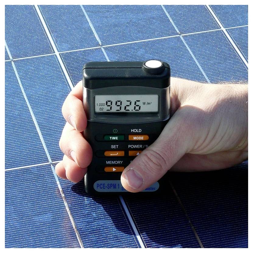 Hand die een zonnestraloingsmeter over een fotovoltaïsch paneel houdt, met een aflezen van 992,6 W/m².
