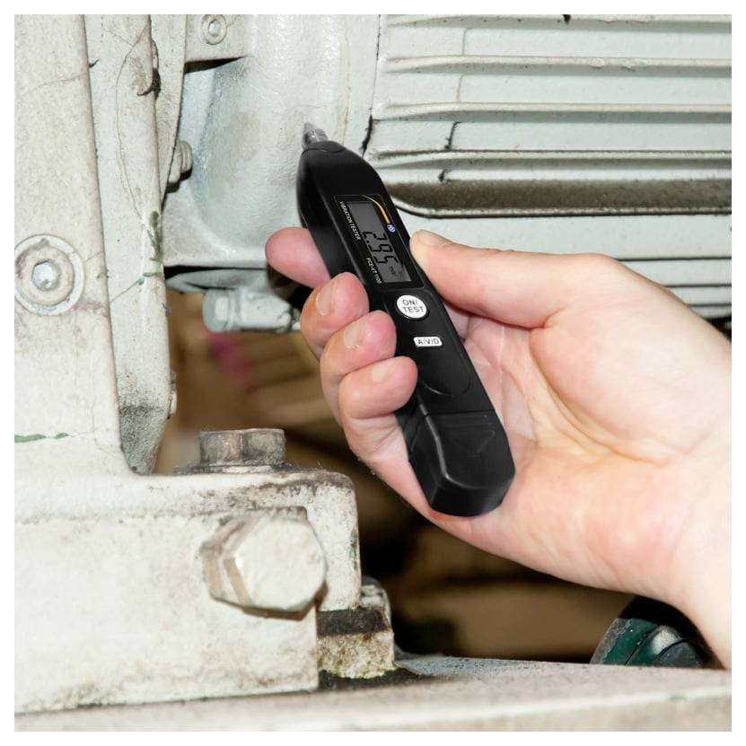 Hand die een digitale infraroodthermometer in de buurt van een metalen machineonderdeel houdt, waarbij de oppervlaktetemperatuur wordt gemeten.