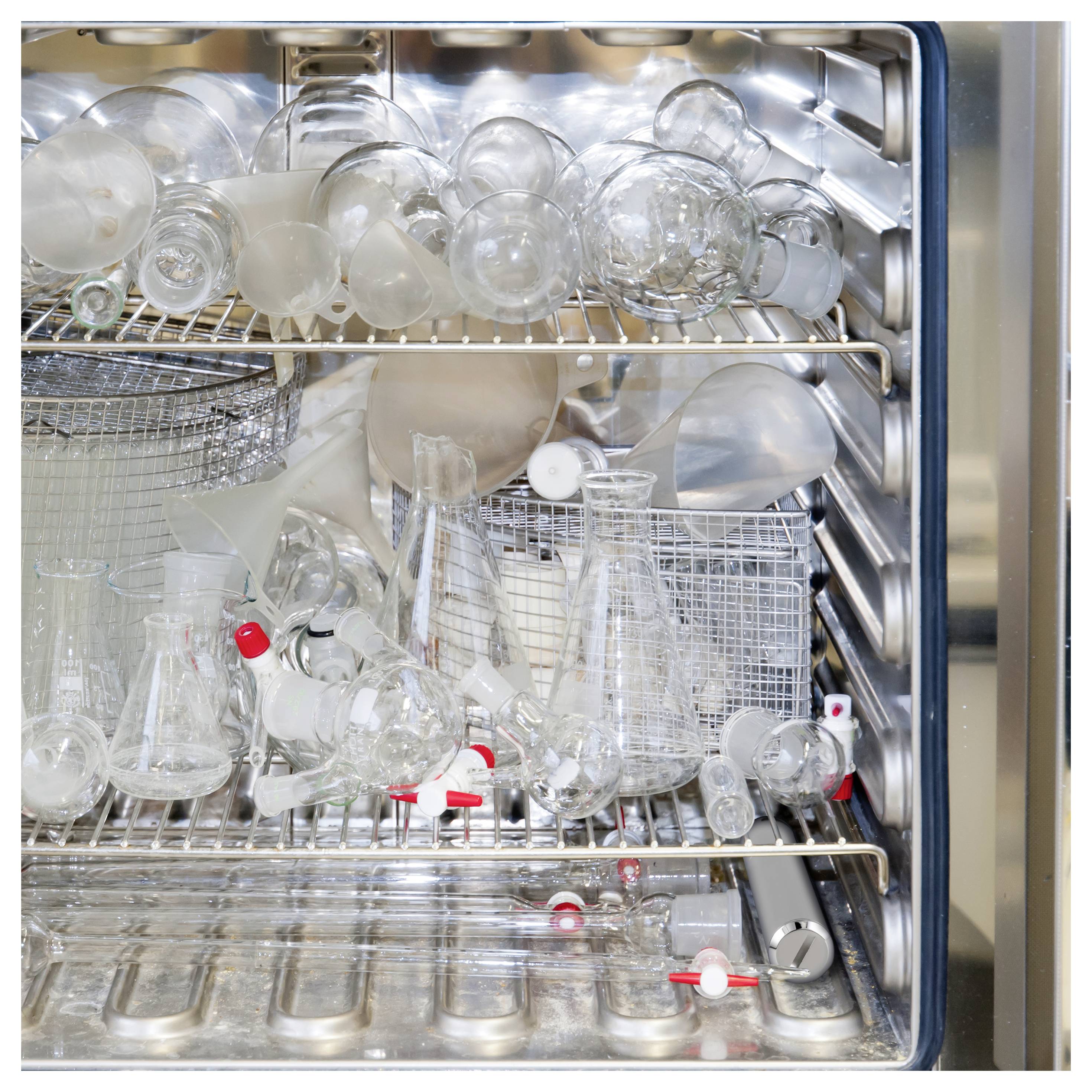 Vaatwasser rek vol met laboratoriumglaswerk en kolven die drogen in een open roestvrijstalen kamer.