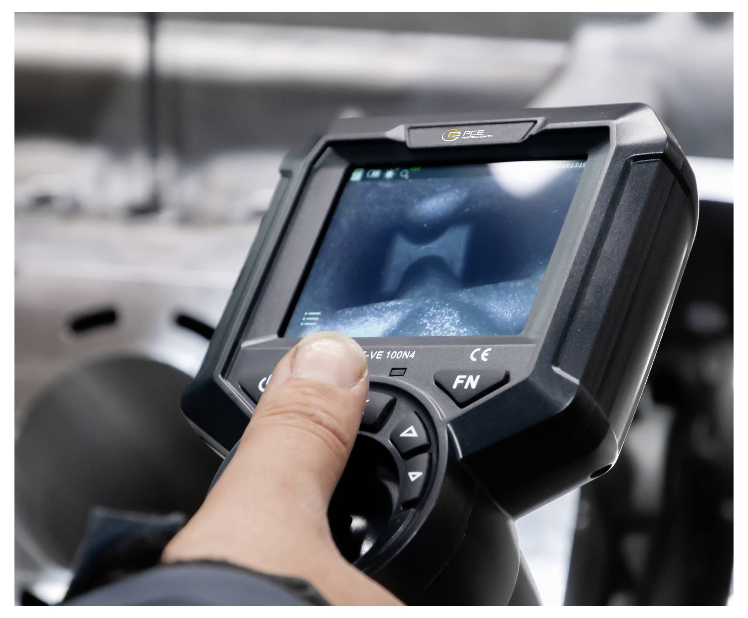 Persoon die knoppen op een draagbaar industrieel apparaat met scherm indrukt, waarschijnlijk een scanner of controller, in een werkplaatsomgeving