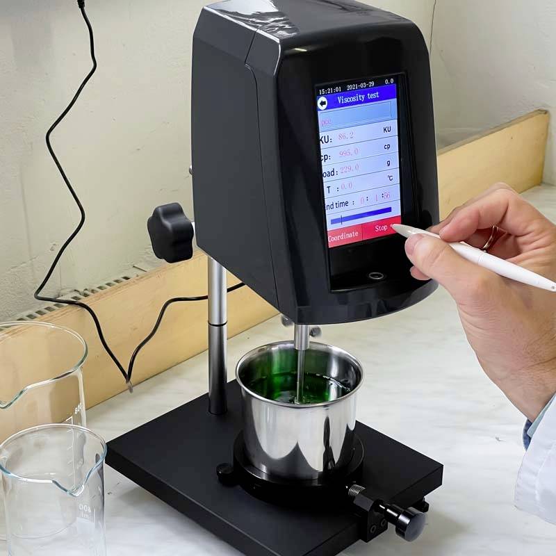 Een hand bedient een viscosimeter die de viscositeit van een groene vloeistof meet. Een display toont de testresultaten.